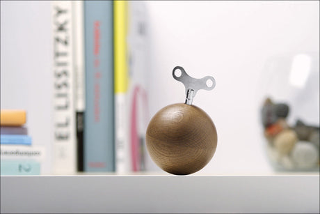 Holzball mit Metallteil auf weißer Oberfläche, im Hintergrund Bücher und eine Figur.