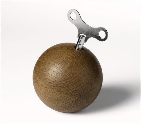Holzball mit einem Metall-Stopfen und einem Metall-Teil, das wie ein Schraubenschlüssel aussieht, auf einem weißen Hintergrund.