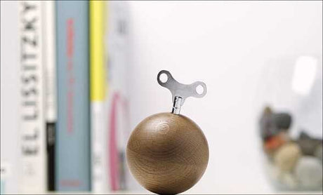 Holzball mit Metallklemme auf einem Regal, im Hintergrund Bücher und Gegenstände.
