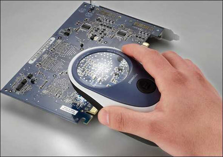 Hand hält Lupe über eine Computer-Hardware-Komponente auf einer Platine.