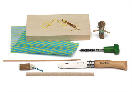 Verschiedene Werkzeuge und Materialien, darunter Messer, Holzstücke, Draht, Stoff, Holzblock, kleine Figur aus Holz und Schnur.