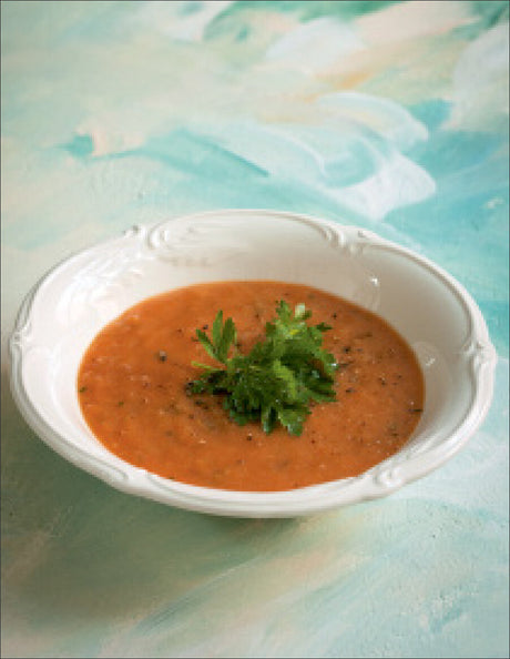 Tomatensuppe mit Petersilie in einer weißen Schale auf einem bunten Hintergrund.