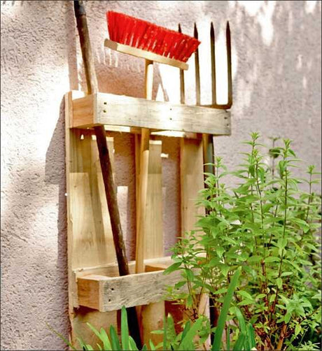 Gartenwerkzeughalter aus Holz mit Rechen, Hacke, Gartenschlauch und Pflanze.