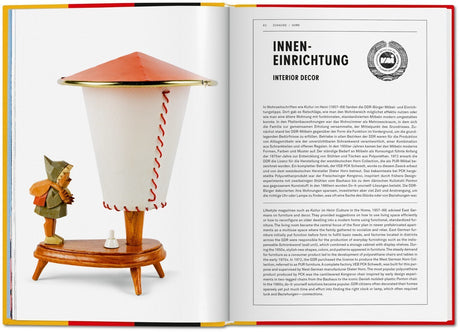 Lampenschirm in Form eines umgedrehten Papiers, mit Holzsockel und kleiner Figur daneben.