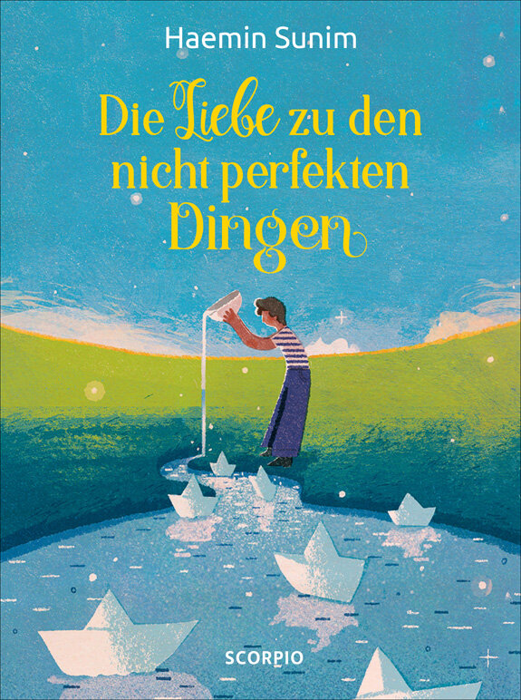 Buchcover mit einem Jungen, der Papierboote in einem Fluss mit grüner Wiese im Hintergrund baut.