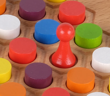 Roter Spielstein in der Mitte, umgeben von bunten, runden Spielsteinen auf Holzbrett.