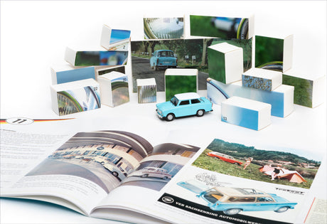 Miniaturmodell eines blauen Autos, umgeben von aufgestellten Fotokarten und einem offenen Buch mit Auto-Fotos.