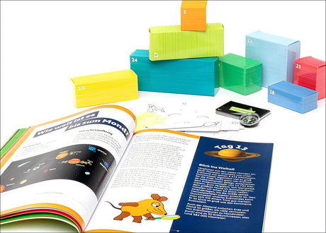 Offenes Kinderbuch mit Weltraum- und Tierbildern, bunte Bauklötze, Kompass, Stift und Papier.