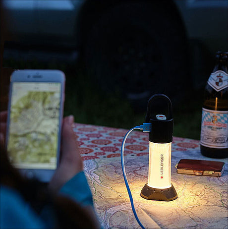 Tisch mit Karte, LED-Laterne, Smartphone, Bierflasche und Geldbörse bei Dämmerung.