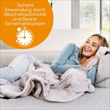 Frau liegt entspannt auf einem Sofa, lächelt, hält ein Kissen und ist von einer Decke zugedeckt.