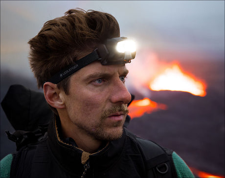 Mann mit Stirnlampe vor ausbreitender Lava bei Sonnenuntergang.