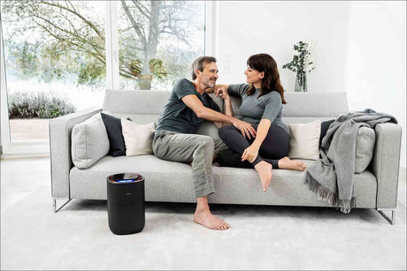Ein Mann und eine Frau sitzen auf einem grauen Sofa, lachen und schauen sich liebevoll an.