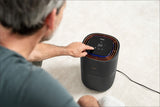 Ein älterer Mann sitzt auf dem Boden und bedient einen schwarzen Luftreiniger mit Touchscreen-Display, das 60°C anzeigt.