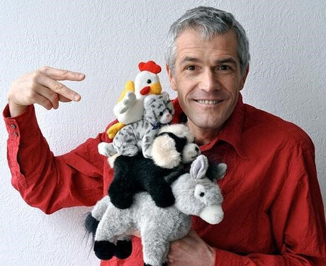Ein Mann in rotem Hemd hält eine Handvoll Plüschtiere, darunter eine Ente, ein Zebra, einen Hasen und einen Hund, vor sich.
