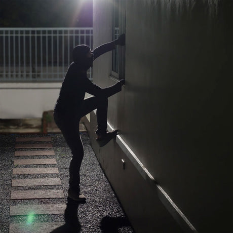Silhouette eines Kindes beim Klettern an einer Hauswand bei Nacht, im Hintergrund eine weiße Metallzaun.
