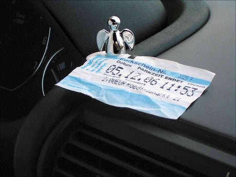 Parkticket mit Datum und Uhrzeit, eine kleine silberne Engel-Figur, auf einem Autocockpit.