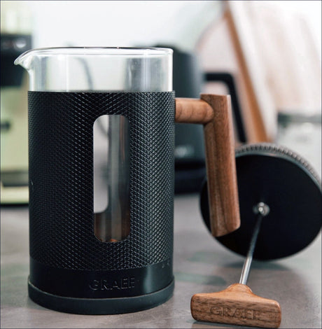 Kaffeemühle mit Holzgriff und Glasbehälter, auf einem Tisch.