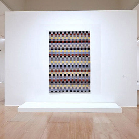 Hängendes Wandbild mit geometrischem Muster aus bunten Quadraten in einem Museum.