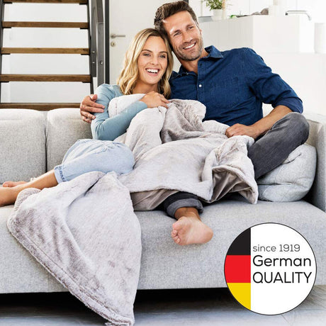 Ein lachendes Paar sitzt auf einem Sofa, die Frau ist schwanger, beide umarmen sich.