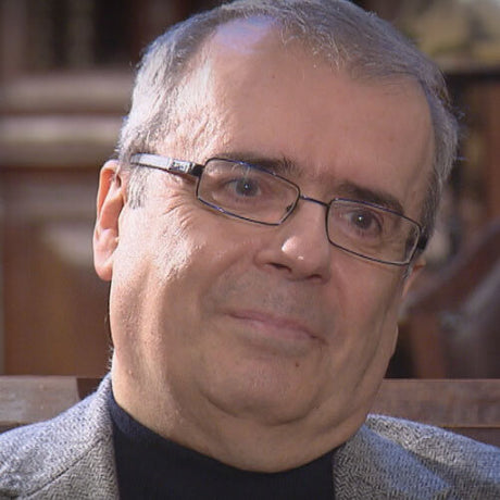 Ein Mann mit Brille, grauem Haar, trägt einen schwarzen Rollkragen und eine graue Jacke.