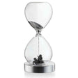 Ein Sanduhr mit schwarzem Sand, der im oberen Teil läuft und im unteren Teil eine kleine Pflanze oder Zweig liegt.