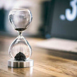 Ein Sanduhr mit schwarzem Sand, die auf einem Holztablett steht.