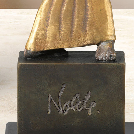 Skulptur mit goldener Robe, nur die Füße sichtbar, auf einem schwarzen Sockel mit der Unterschrift "Nolde".