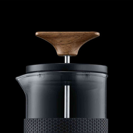 Kaffeemühle mit Holzknopf, transparentem Glasbehälter und schwarzem Griff vor schwarzem Hintergrund.