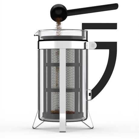 A French press mit Kaffeebohnen im Filter, schwarzer Löffel darüber, auf weißem Hintergrund.