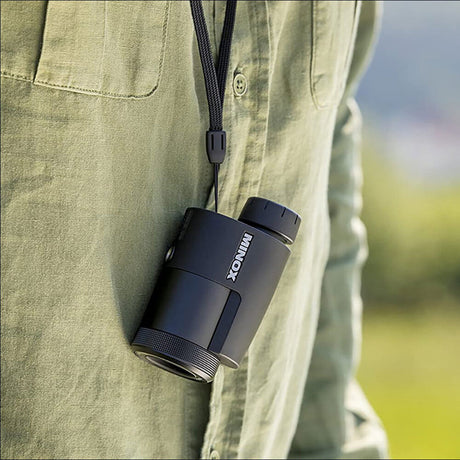 Kleiner schwarzer Monokular mit "MINOX"-Logo, um den Hals gehängt, an grünem Hemd.