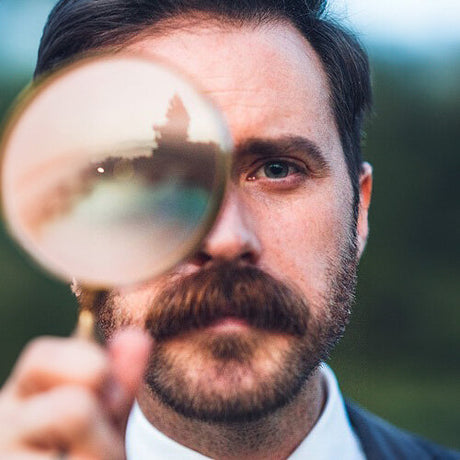 Mann mit Brille, Blick durch Lupenlinse, unscharfer Hintergrund, Nahaufnahme.