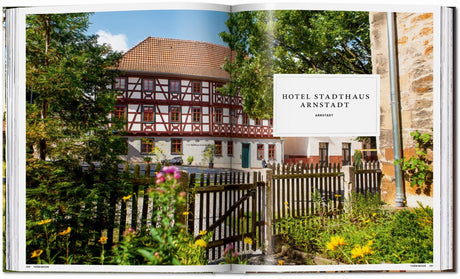 Historisches Fachwerkhaus mit rotem Dach, umgeben von Bäumen und Blumen, mit Schild "Hotel Stadthaus Arnstadt".