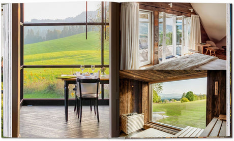 Innenansicht eines Hauses mit großen Fenstern, Blick auf grüne Wiesen und Berge, mit Essbereich, Balkon und Sauna.